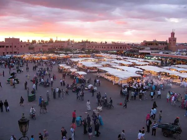 Is Marrakech safe at night ? nighttime view of Jemaa el-Fna Square with market stalls, palm trees, and the Koutoubia Mosque minaret