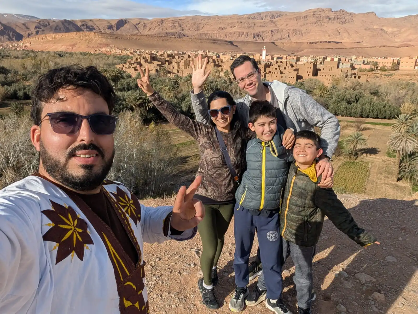 Is Morocco safe for families with children? A happy family of four poses with their private driver-guide overlooking a Berber village in the Atlas Mountains.