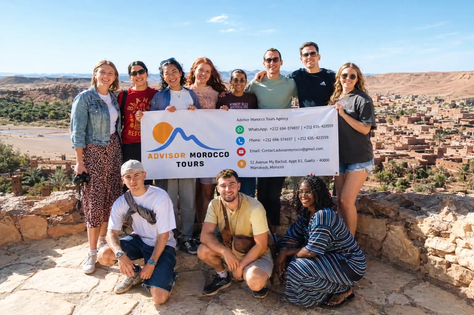 Morocco visa for Colombians: group of travelers holding an Advisor Morocco Tours banner in a Moroccan desert village