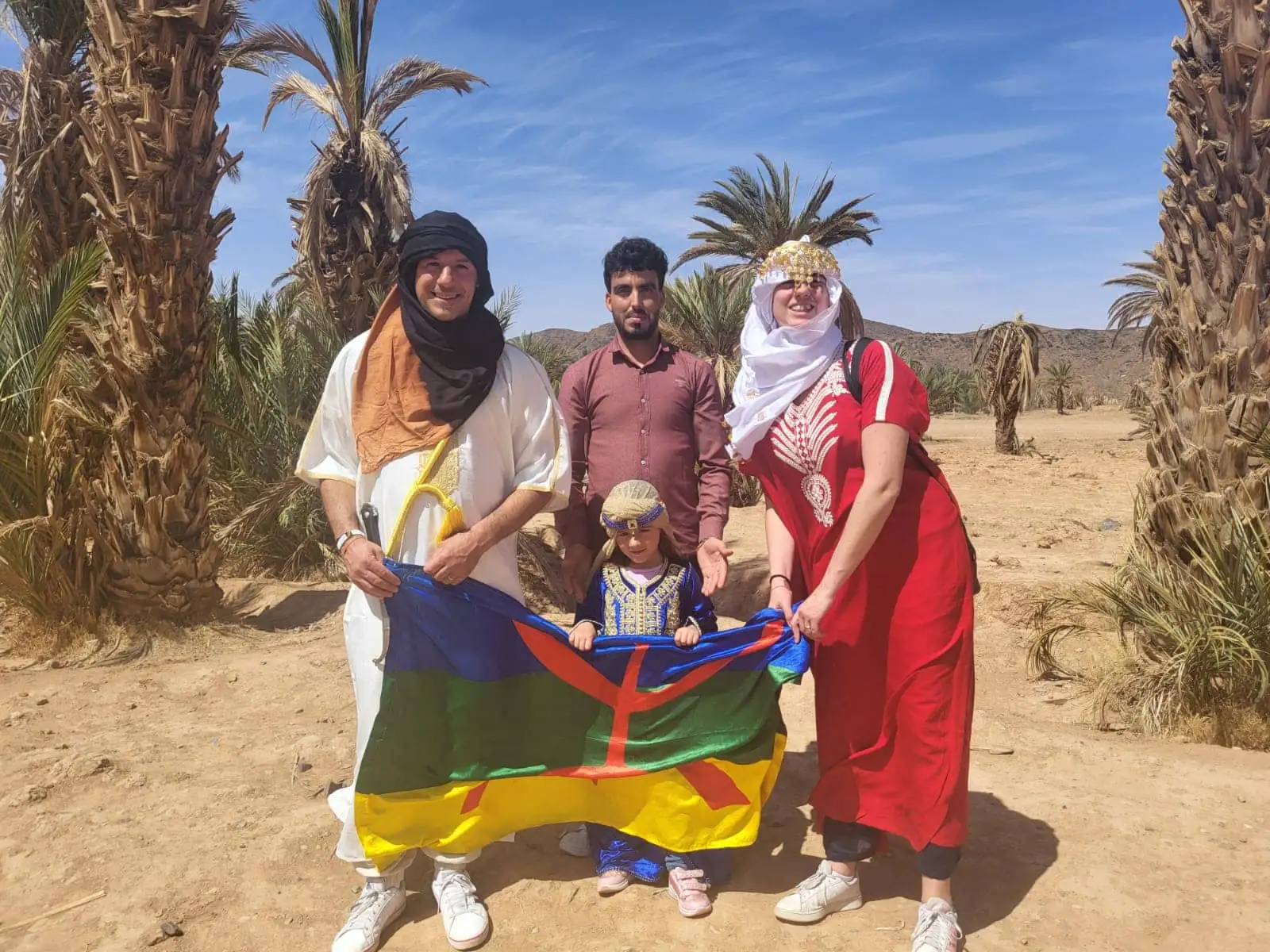 What you should know about Moroccan people: a group in traditional Amazigh clothing holding the Amazigh flag in a palm oasis