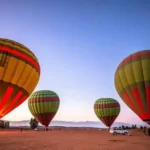 Hot air balloon ride in Marrakech with multiple colorful balloons inflating at sunrise in the desert near the Atlas Mountains