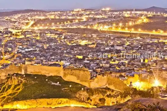 Is Fes safe at night? Aerial view of Fes Medina lit up at dusk with the historic city walls