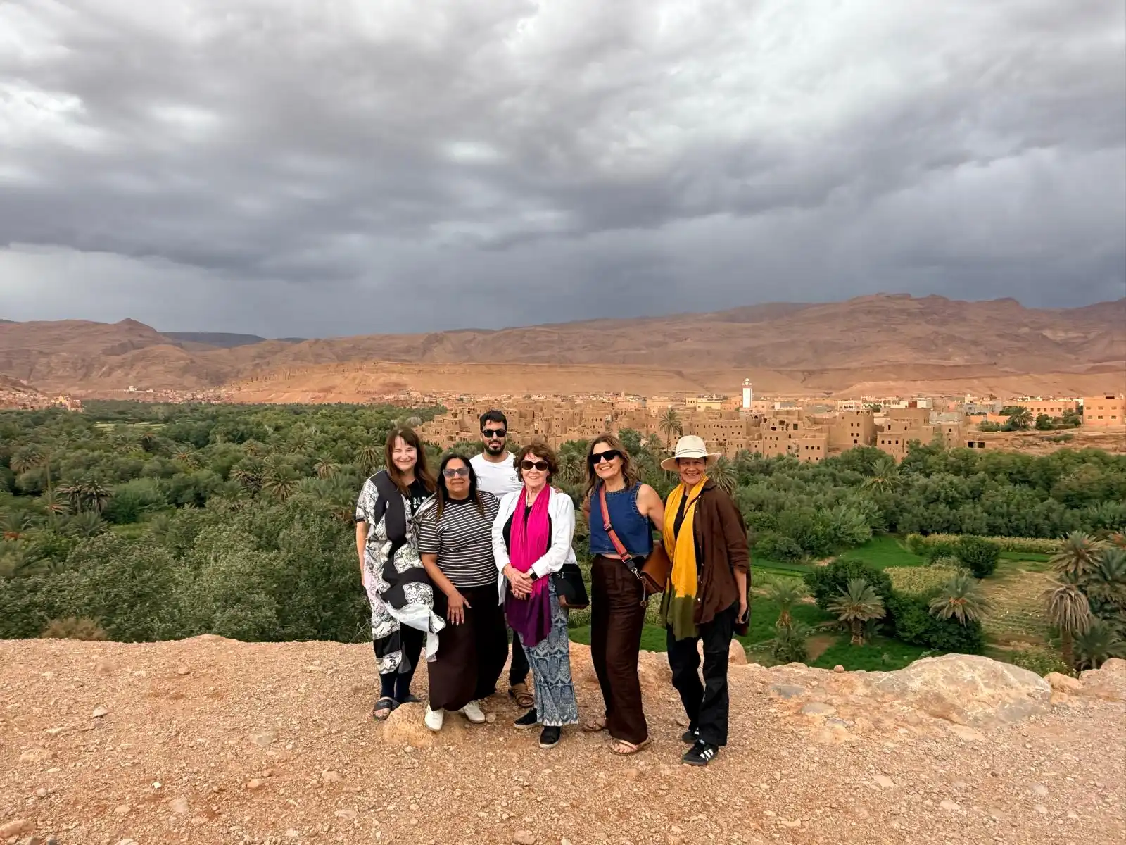 Travelers enjoying a Tangier to Sahara Desert Tour in Morocco, overlooking a palm oasis and traditional village.